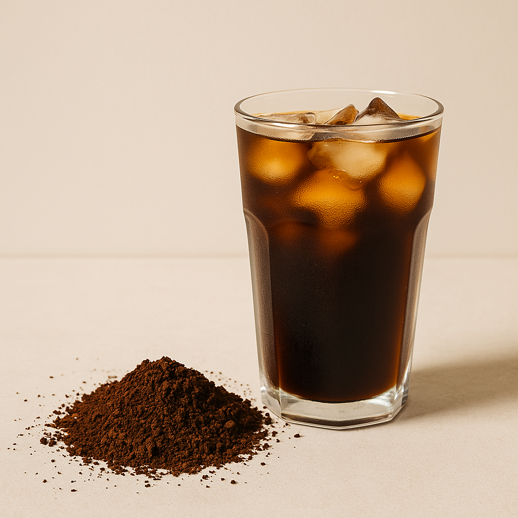 Stiklinė su Cold Brew kava ir ledo kubeliais ant šviesaus fono, šalia malta kava – NUVO Cold Brew gidas.